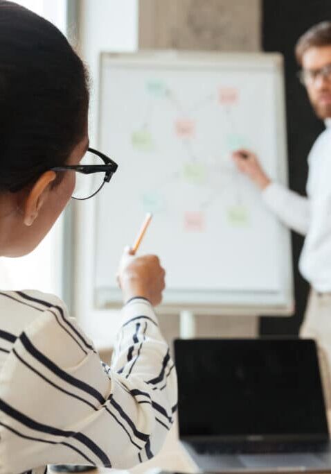 Image of young business man showing project on desk to his colleagues indoors coworking. Focus on african woman pointing to desk.